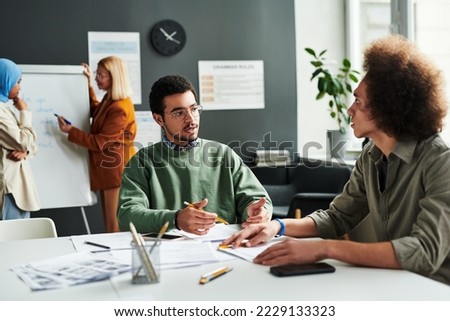Young confident Middle Eastern male student talking to other learner at lesson of foreign language against teacher and Muslim woman Royalty-Free Stock Photo #2229133323