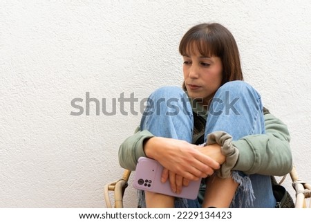worried and sad girl with a shrug position. Girl leaning her elbows on her knees with the mobile in her hands with a lost look and a sad reaction Royalty-Free Stock Photo #2229134423