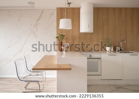 Modern and minimalist kitchen with white furniture, wooden elements and marble floor and wall Royalty-Free Stock Photo #2229136355