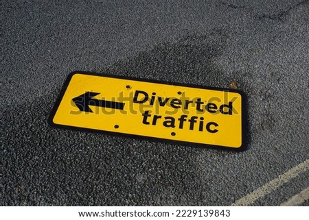 Diverted traffic road sign laying flat on road surface. yellow road sign in UK.