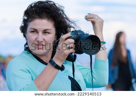 A brunette woman with a photo camera in her hands.