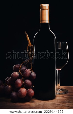 A glass of red wine and a bottle and grape.