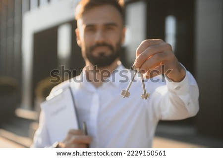 Real estate agent holding key on blurred background, closeup. Royalty-Free Stock Photo #2229150561
