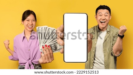 Excited asian spouses young woman and middle aged man celebrating success on yellow, betting on Internet, showing smartphone with white empty sceen and money, clenching fists, mockup, collage