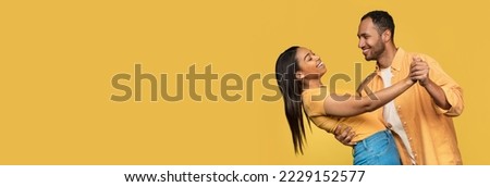 Place For Ad. Happy Young Black Couple Dancing Together Over Yellow Background, Cheerful African American Man And Woman Having Fun And Looking To Each Other, Wide Horizontal Banner With Copy Space Royalty-Free Stock Photo #2229152577