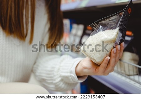Female consumer holding white rice pack, shopping dry food,girl buying jasmine rice in transparent plastic bag,choose raw rice products packed for sell at supermarket,food nutrition Royalty-Free Stock Photo #2229153407