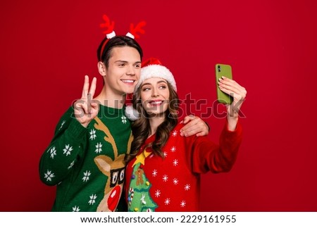 Portrait of two cheerful funny people hug make selfie show v-sign santa headwear deer antlers isolated on red color background
