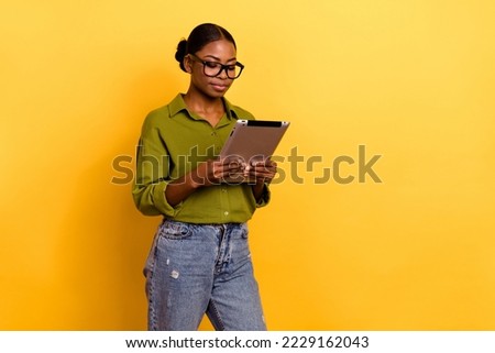 Portrait of attractive focused girl using gadget reading e-book isolated over bright yellow color background