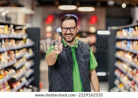 A happy hypermarket manager is standing at marketplace and showing thumbs up at the camera and smiling. Royalty-Free Stock Photo #2229162535