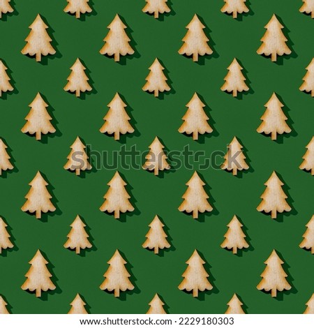 Large and small wooden fir tree silhouettes over green background. Christmas and New Year seamless pattern. Winter holidays design element in yellow green colors. Hard light shot. Top view.