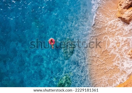 Aerial top view young woman swimming with donut pink inflatable swim ring in blue sea. Concept tropical paradise travel relax.