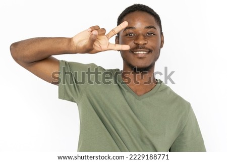 Smiling young man making peace sign near his face. Male African American model in green T-shirt smiling and showing peace sign near his face with fingers. Emotions, victory concept.