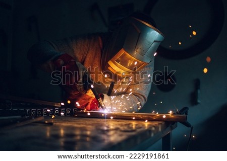 Man worker working with a metal product and welding it with a arc welding machine in a workshop. Industrial manufacturing. Welding metal part in a factory. Orange sparks. Copy space. Royalty-Free Stock Photo #2229191861