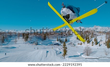 CLOSE UP: Stunning view of freestyle skier doing grab trick while jumping kicker. Young extreme athlete flying high above snow park and ski area. Adrenaline activity on sunny winter day in ski area. Royalty-Free Stock Photo #2229192395