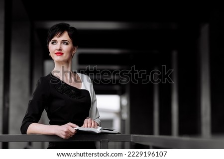 Businesswoman with red lipstick on lip is working with paper notebook on office building in the background. Executive is resolving work issues outdoors. Achievement career wealth business concept