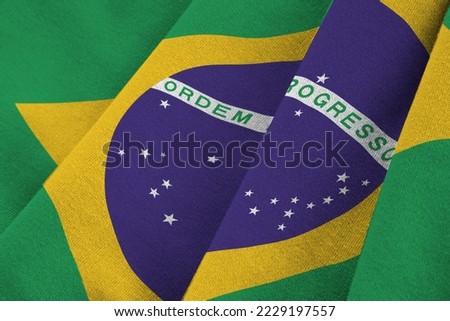 Brazil flag with big folds waving close up under the studio light indoors. The official symbols and colors in fabric banner