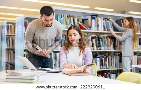 Male and female university students working on laptop computer in library, reading books and making notes, preparing to exam