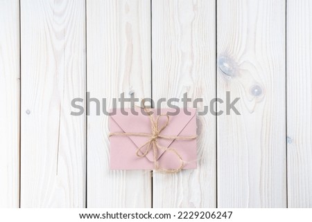 Pink envelope tied with rough jute rope on white wooden background. Copy space. Top view. Mail, correspondence, sending messages, congratulations