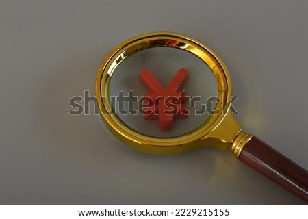 Magnifying glass and Japanese Yen currency symbol isolated on a grey background