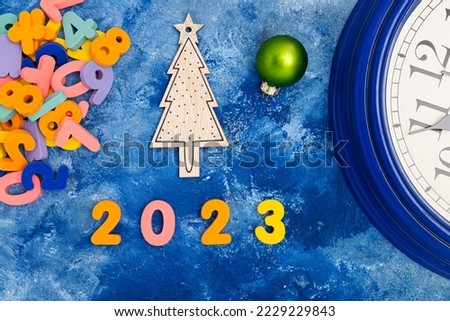 New Year composition with Numbers 2023 and clock. Christmas decorations on blue background. View from above.