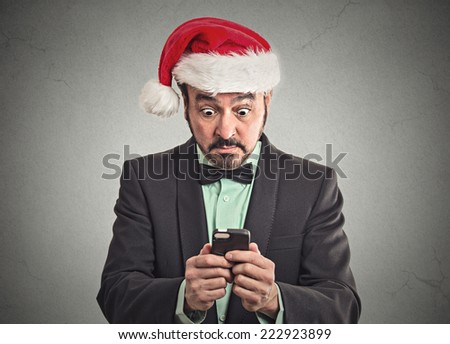Portrait surprised funny business man wearing red santa claus hat looking at smart phone shocked discovered great online deal sale. Human emotion facial expression body language. Holiday season