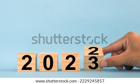 Hand flipping wooden cubes blocks on blue background for change year 2022 to 2023. New year and holiday concept.