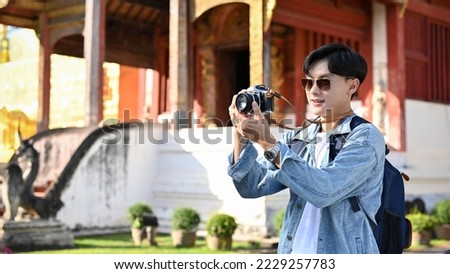 Handsome young Asian male traveler talking a picture of beautiful ancient Thai-Northern temple by his retro camera. Asia, Chiang Mai, Thailand traveling and vacation concept