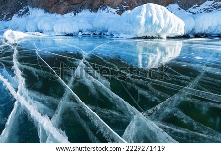 Natural winter background with beautiful Baikal ice on frosty February day. Close-up view on smooth blue ice with cracks and coastal rocks with thick ice crust. Winter travel and outdoor recreation Royalty-Free Stock Photo #2229271419