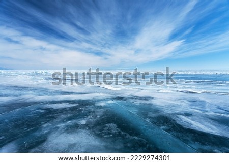 Unusual winter landscape of frozen Baikal Lake on February day. Above icy endless desert, beautiful stratus clouds adorn the blue sky. Natural cold background. Winter travel and outdoor recreation Royalty-Free Stock Photo #2229274301