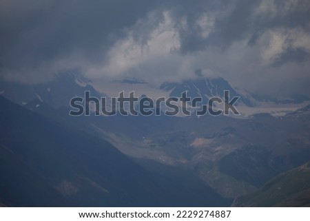 Dark atmospheric surreal landscape with a dark rocky mountain peak in low clouds in a gray cloudy sky. A gray low cloud on a high peak. High black rock in low clouds. Surreal gloomy mountains.
