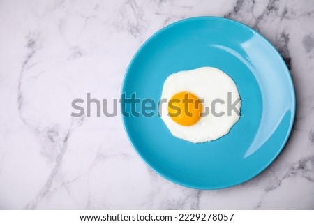 Tasty fried egg in plate on white marble table, top view. Space for text