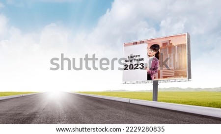 Asian businesswoman showing a board with a new year greeting on the billboard beside the street. Happy New Year 2023