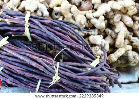 bunches of Purple-pod Xpelon beans on fresh Ginger root on a market stall