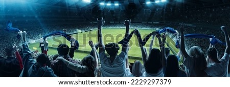 Back view of excited football, soccer fans cheering their team with blue scarfs at crowded stadium at evening time. Concept of sport, cup, world, team, event, competition Royalty-Free Stock Photo #2229297379