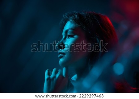 Portrait of young beautiful woman posing isolated over blue studio background in neon light. Side view photography. Concept of youth culture, emotions, facial expression, fashion. Copy space for ad