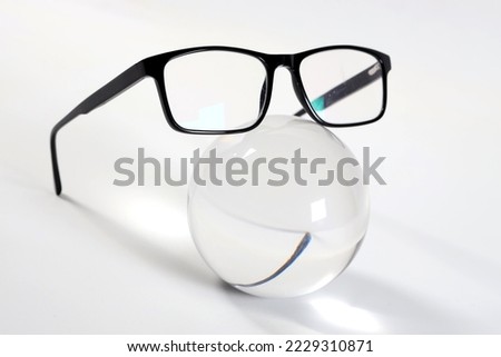 modern elegant dark-framed glasses on a white background next to a glass sphere