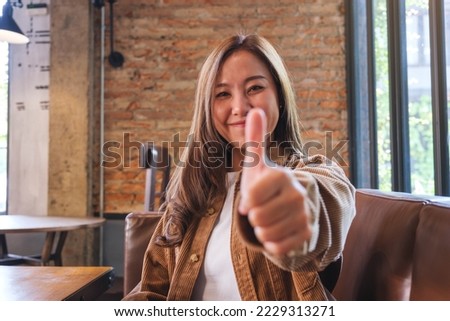 Portrait image of a young asian woman making and showing thumbs up hand sign