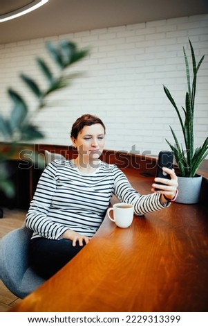 A woman sits at a table in a modern office and communicates on a smartphone