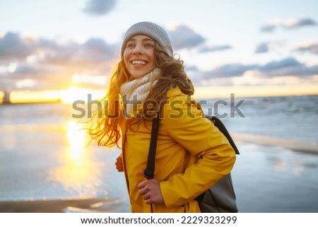 Happy tourist in a yellow jacket posing by the sea at sunset. Travelling, lifestyle, adventure. Royalty-Free Stock Photo #2229323299