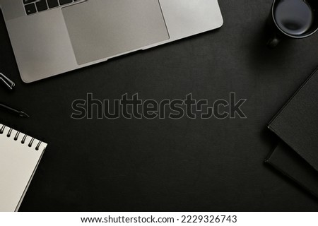 Modern office desk top view, flat lay with copy space for your text display in the middle, laptop, coffee cup, books and stationery on black background.
