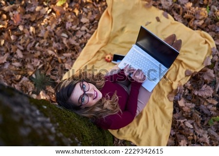 Young businesswoman working on her laptop while enjoying a beautiful autumn day outdoors in the forest