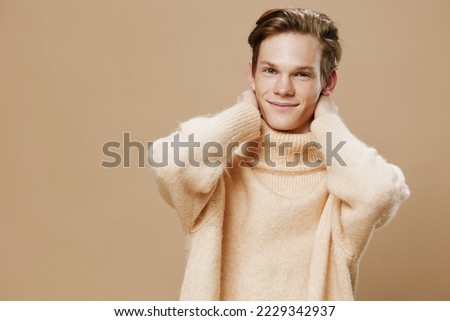 close portrait of a handsome young guy with freckles in a beige textured high neck sweater raising his elbows to the camera