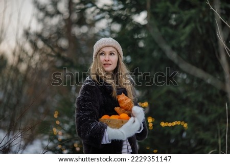 woman under a Christmas tree in the forest before Christmas holds a dish with croissants and oranges in her hands against the background of a decorated Christmas tree