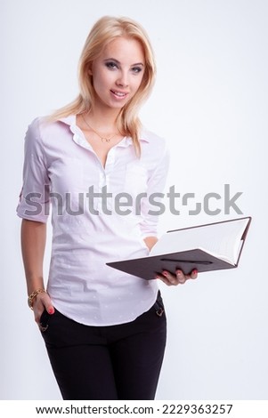 Portrait of a  young adult attractive blonde businesswoman in pink shirt reading notebook on light backround