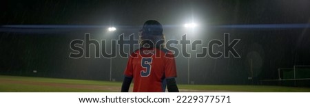 Caucasian kid boy baseball player posing on against flood lights a rainy evening. Shot with anamorphic lens