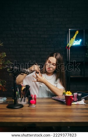 Cute lady beauty blogger is sitting at the table in the studio for shooting and testing makeup for a cameo while recording a lesson.