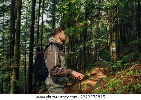 Photo of a male tourist with a stick in his hand in the mountains walking along a path and looking away. Travel in the mountains.