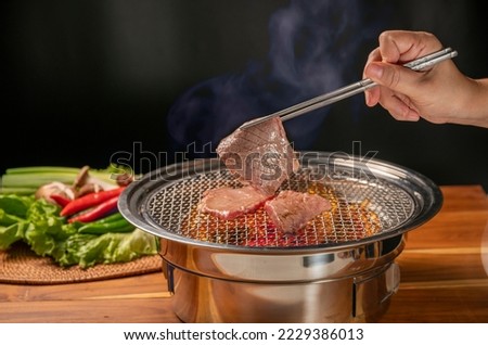 Hand using chopsticks to pick up wagyu beef on hot charcoal Asian BBQ food style, Grilled Beef Sirloin meat on the charcoal stove,Korean BBQ style. Royalty-Free Stock Photo #2229386013