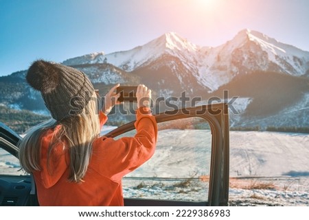 Woman travel exploring, enjoying the view of the mountains, landscape, lifestyle concept winter vacation outdoors. Female with mobile phone standing near the car in sunny day.