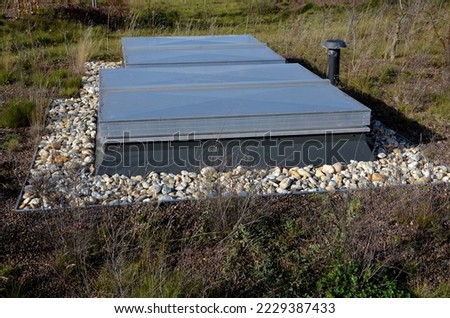 metal grates and a hatch on the roof garden. sheet metal and metal covering the entrances to the back of the cooling units. the area around the door is mulched with pebbles. against fire edge Royalty-Free Stock Photo #2229387433